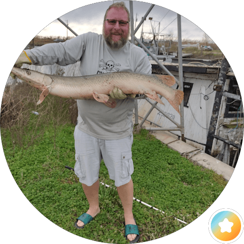 A man stands in grass, proudly holding a large fish he has caught.