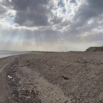 A sandy beach under a cloudy sky featuring a single beach chair positioned on the shore.